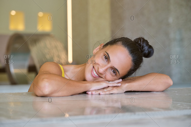 Happy young female looking at camera and smiling while relaxing during spa session with hydro massage in modern wellness center