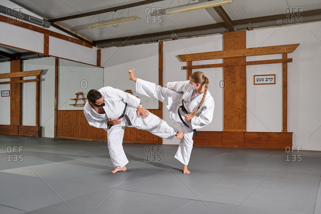 Two people with mask and kimono practicing krav maga kicks during a combat in a gym