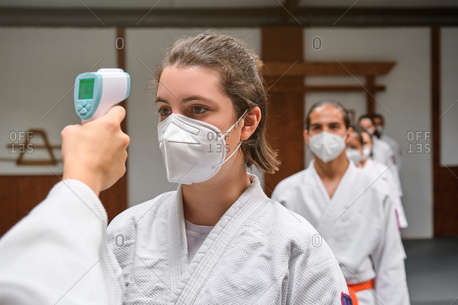 Row of people wearing masks and a kimono taking the covid temperature test in a krav maga gym