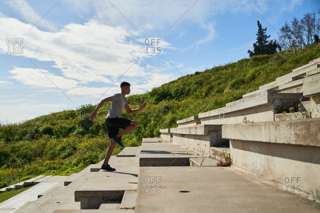 Full body side view of determined young ethnic sportsman running up stairs during intense fitness workout in sunny summer day