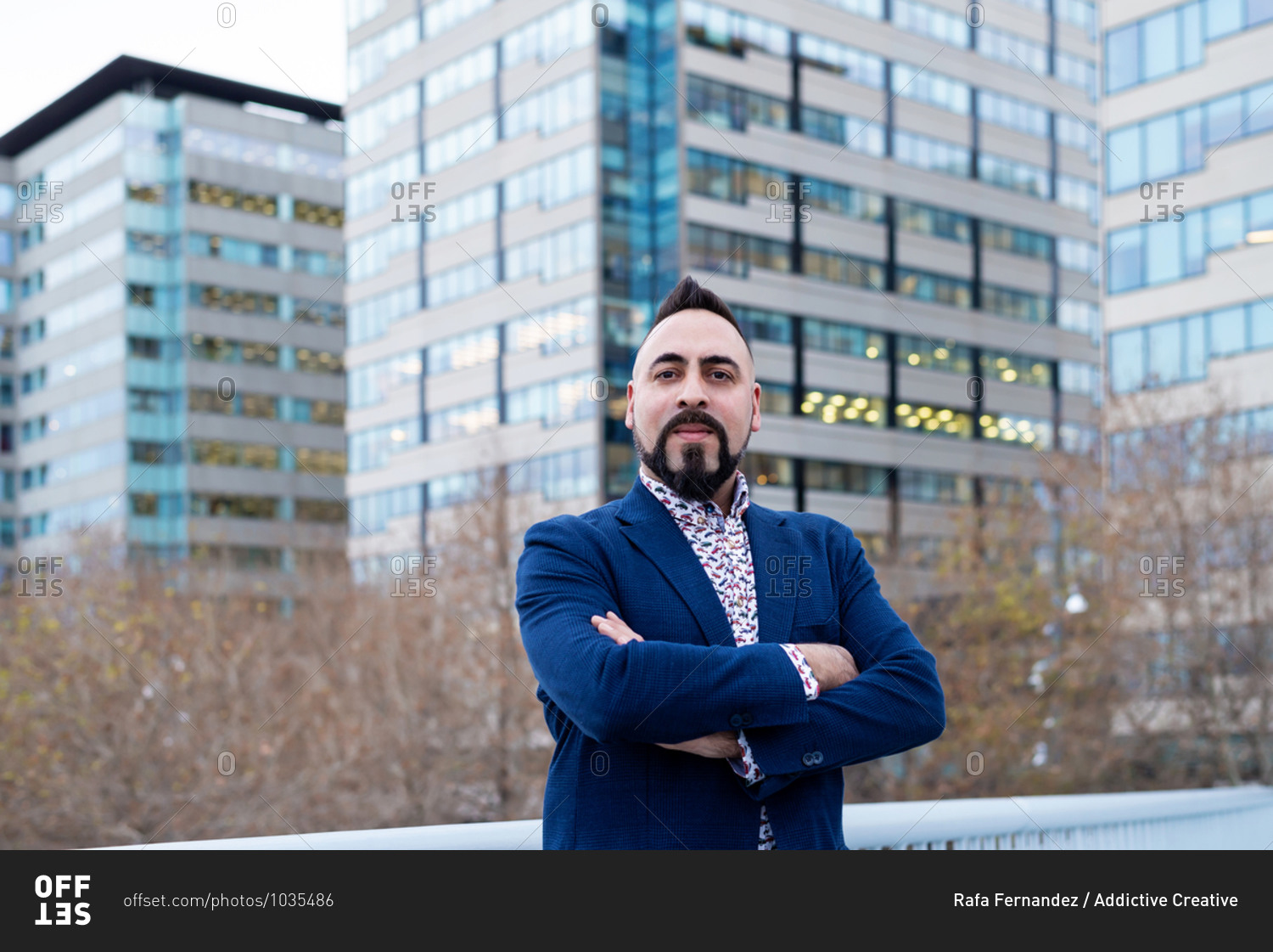 Bearded businessman standing with crossed arms in financial district while looking at camera