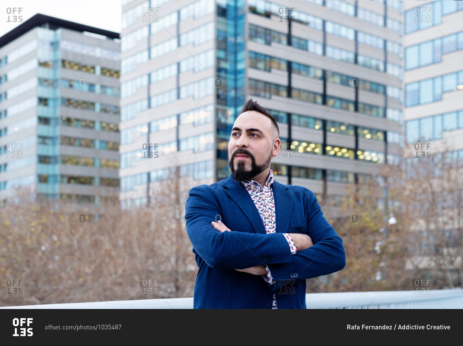 Bearded businessman standing with crossed arms in financial district while looking away