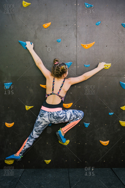 Back view of anonymous child in sportswear climbing wall with artificial rocks while training in gym and enjoying weekend