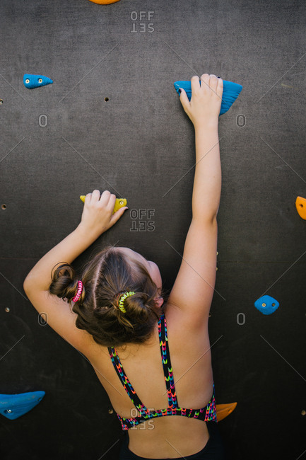Back view of anonymous child in sportswear climbing wall with artificial rocks while training in gym and enjoying weekend