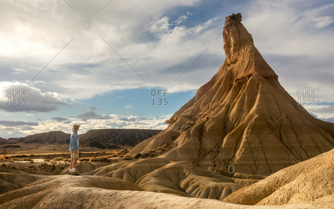 Side view of male tourist in summer wear standing on dried soil in Bardenas Reales and enjoying amazing view of natural rocky formation