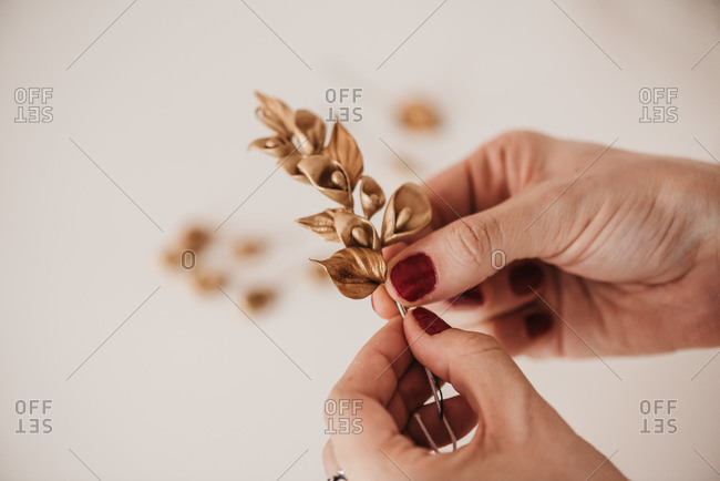 High angle of anonymous female artisan creating decorative flowers and wrapping twig with thread while working in workshop
