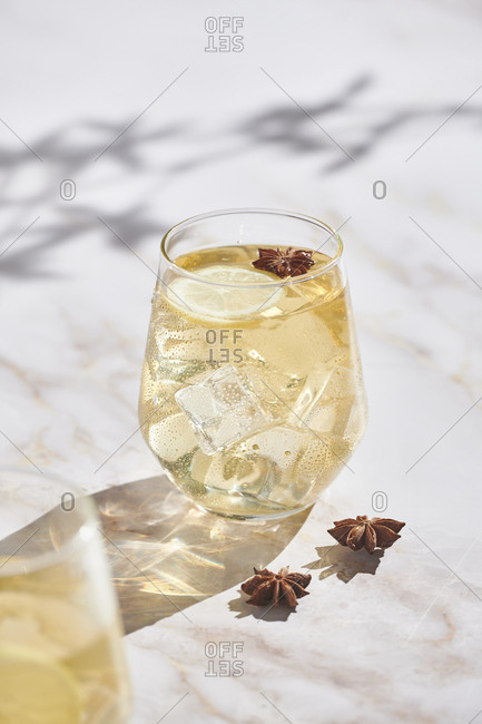 High angle of delicious cocktails with lemon slices and ice cubes garnished with star anise and served on marble table