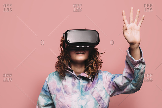 Portrait of redhead girl playing with VR glasses over pink background