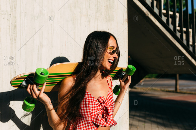 Portrait of brunette girl with long hair holding a long board and looking away in front of white background