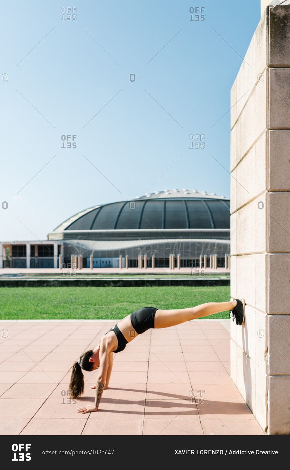 Full body side view of unrecognizable athletic female in sportswear doing feet on wall push ups near concrete building on city square