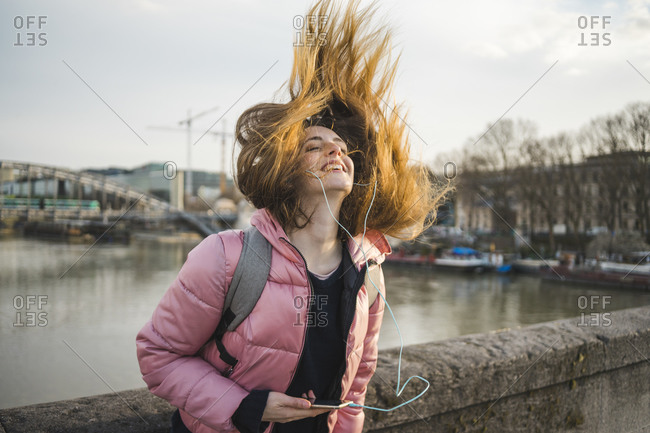 Paris- France- happy young woman listening music with earphones and smartphone tossing her hair