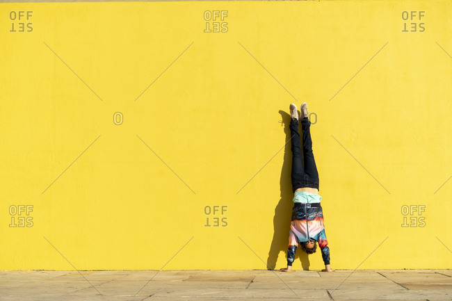 Acrobat doing handstand in front of a yellow wall