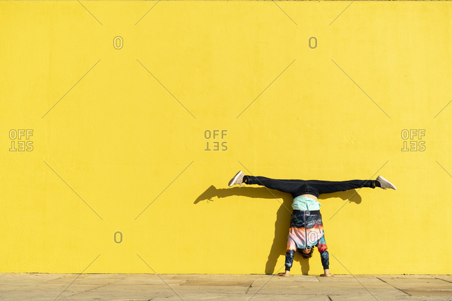 Acrobat doing handstand in front of a yellow wall