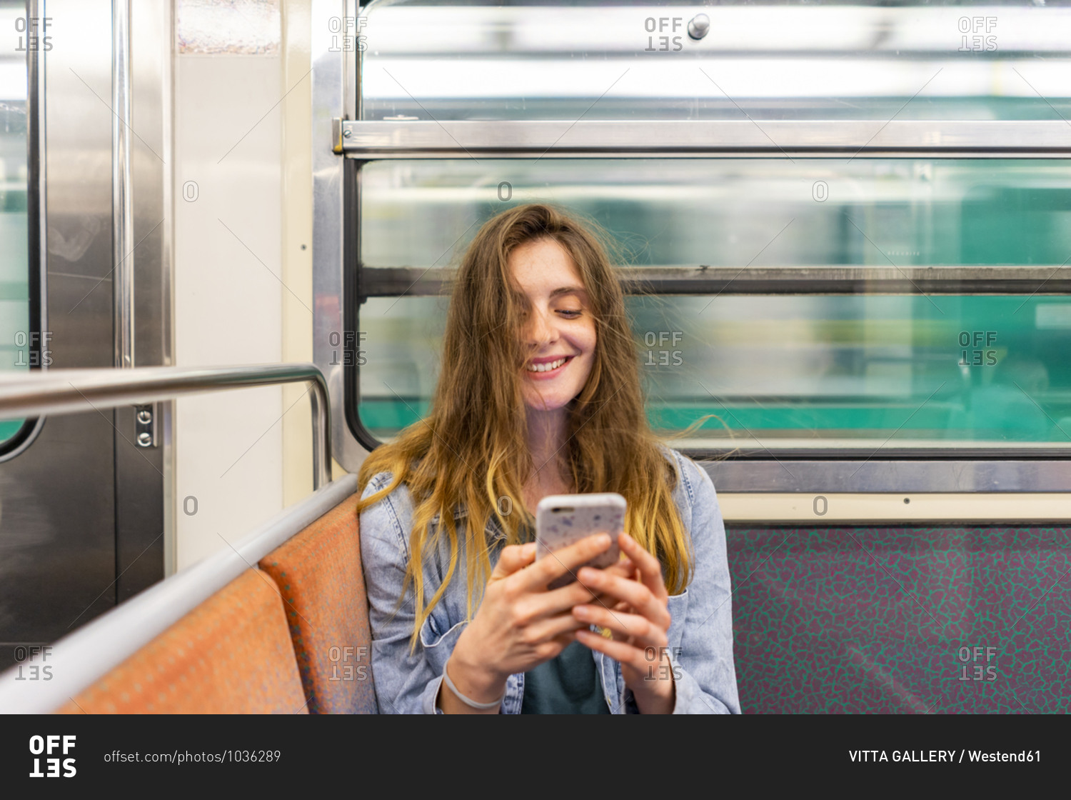 Portrait of smiling young woman in underground train looking at smartphone