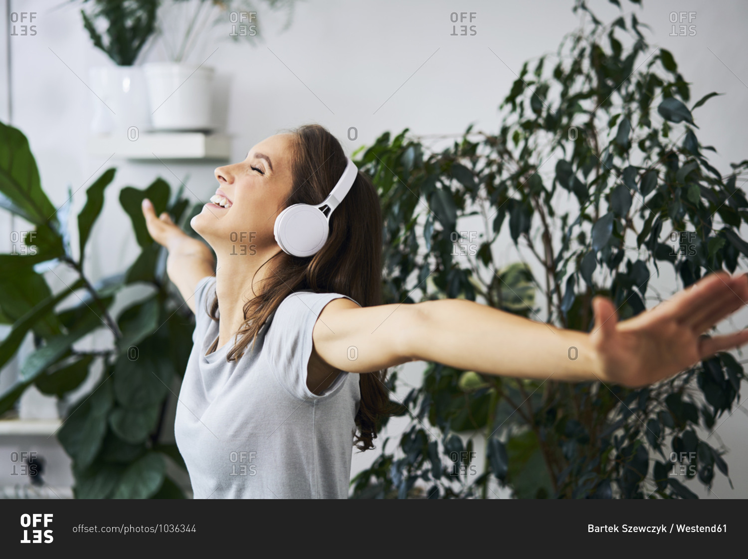 Happy young woman with outstretched arms listening to music at indoor plant