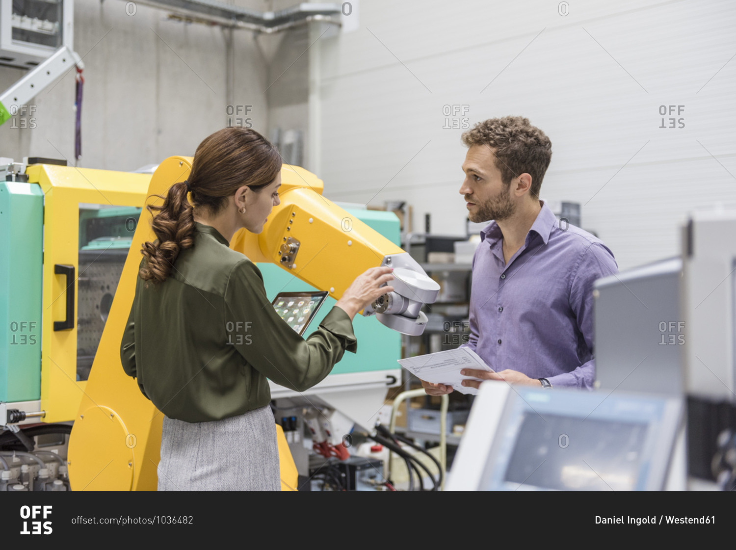 Businessman and woman having a meeting in front of industrial robots in a high tech company