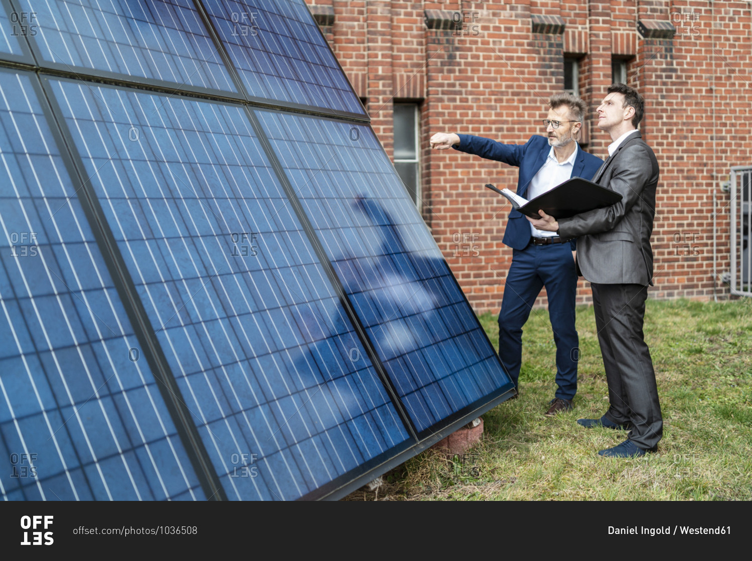 Two businessmen talking outside brick building at solar panels
