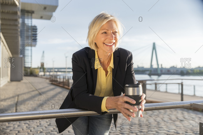 Happy senior businesswoman with takeaway coffee at the riverside
