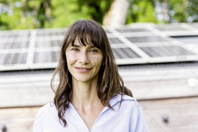 Portrait of smiling woman in front of a house with solar panels on the roof