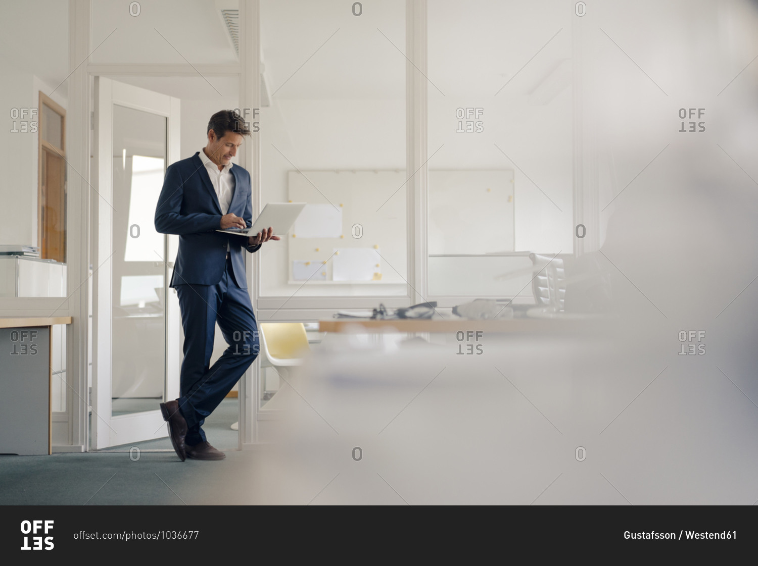Businessman standing in office- using laptop