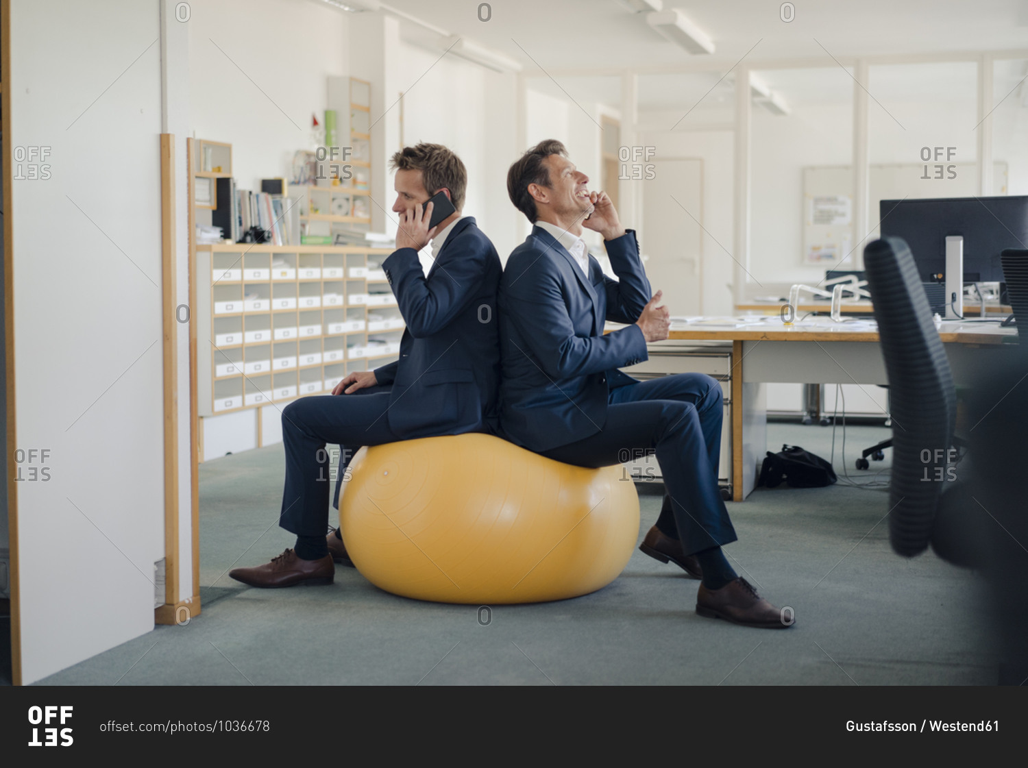 Two businessman checking smartphone with yellow fitness ball in foreground