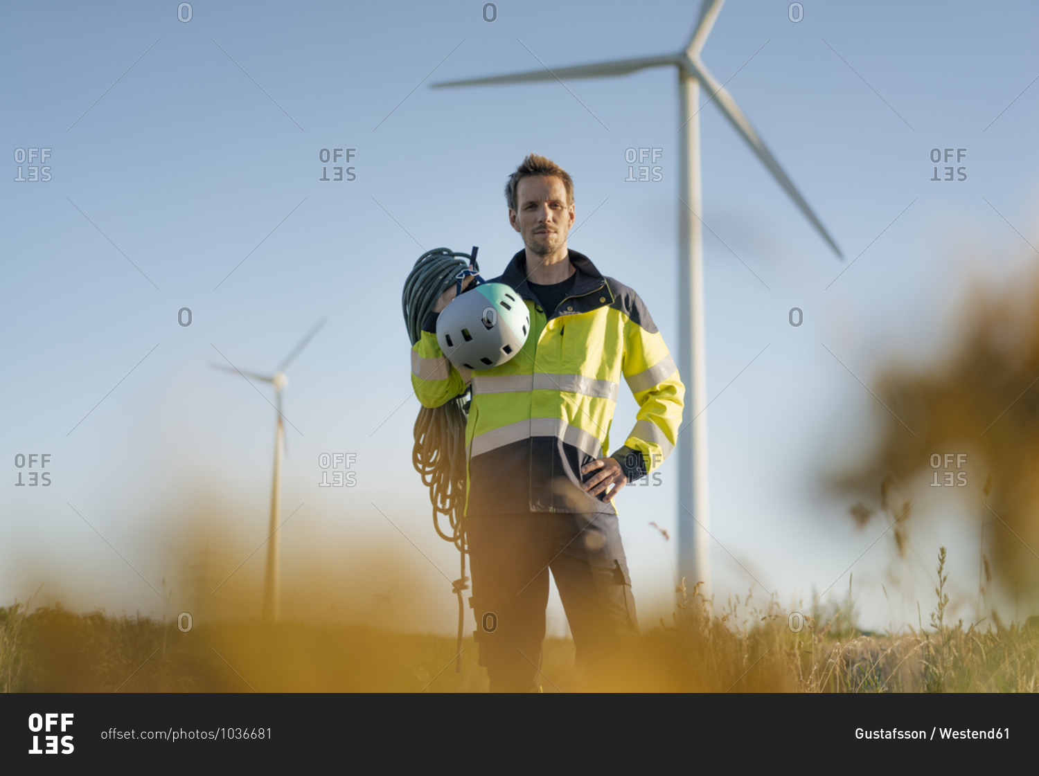 Technician standing in a field at a wind farm with climbing equipment