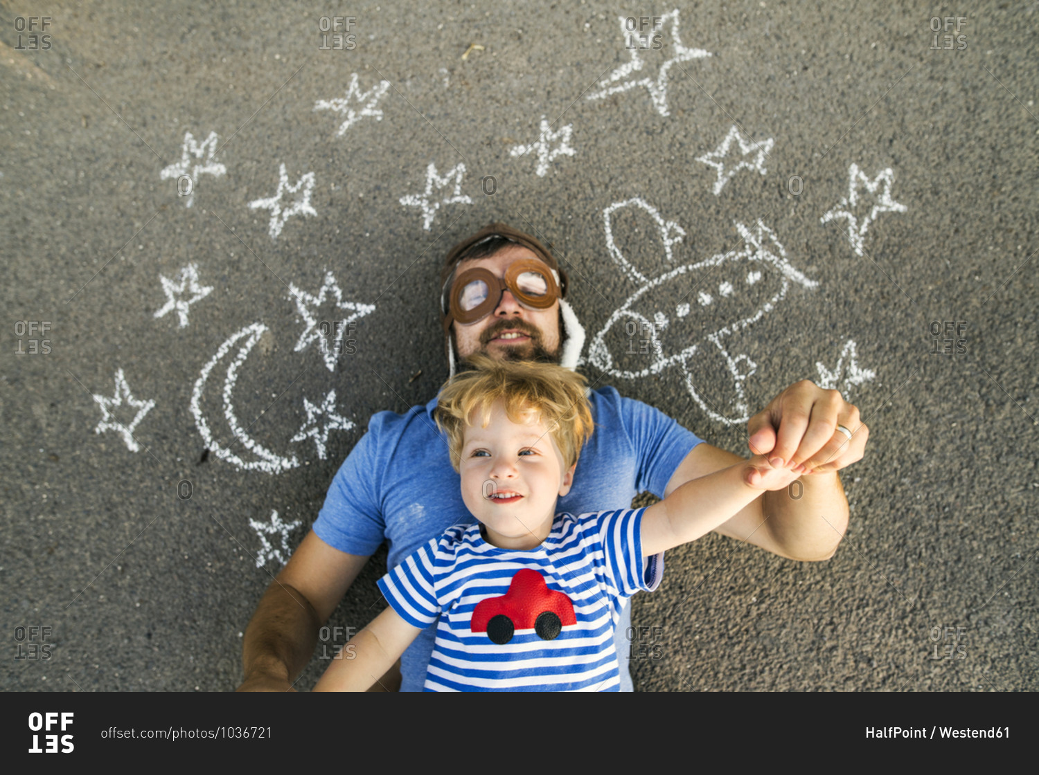 Portrait of mature man wearing pilot hat and his little son lying on asphalt painted with airplane- moon and stars