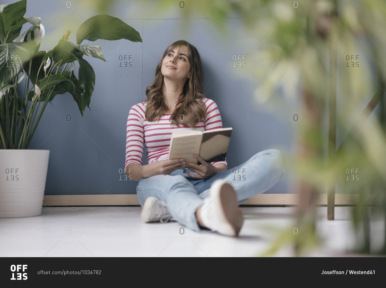 Woman sitting on ground in her new home- reading a book- surrounded by plants