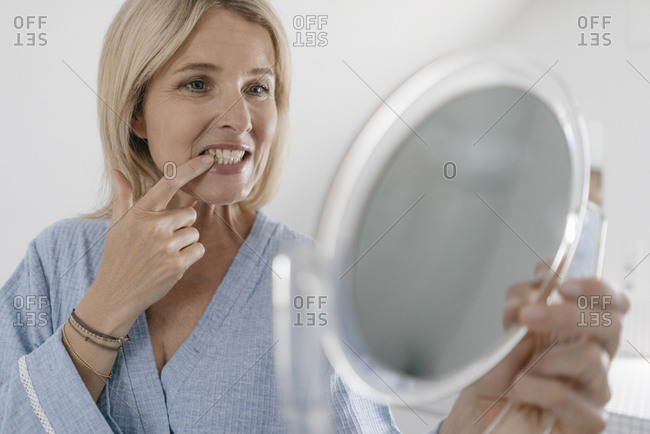 Mature woman looking in beauty mirror in bathroom checking her teeth