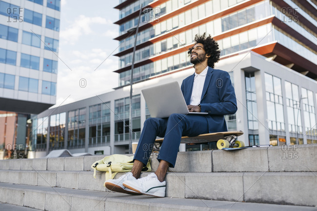 Spain- Barcelona- young businessman sitting outdoors in the city working on laptop