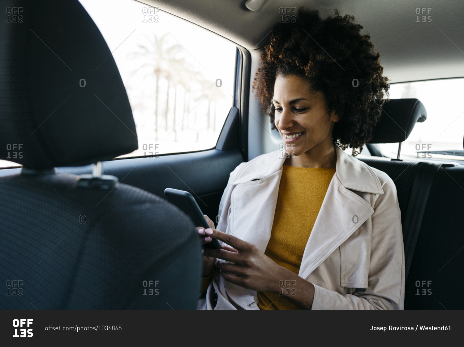 Smiling woman sitting in back seat of a car using cell phone