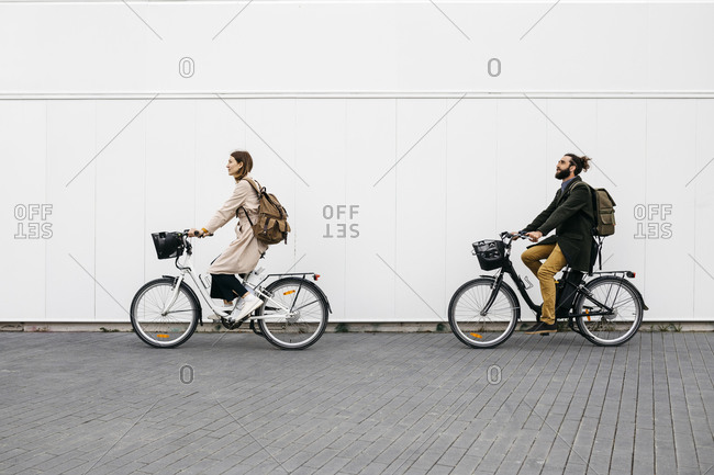 Couple riding e-bikes along a white wall in the city