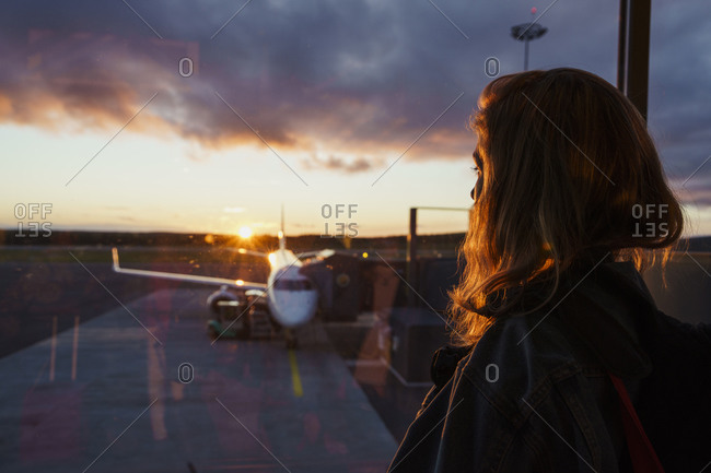 Young woman looking through window on plane at the airport at sunset