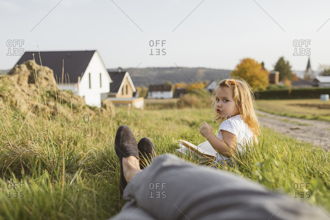 Portrait of little girl sitting on a meadow with a book looking at her mother