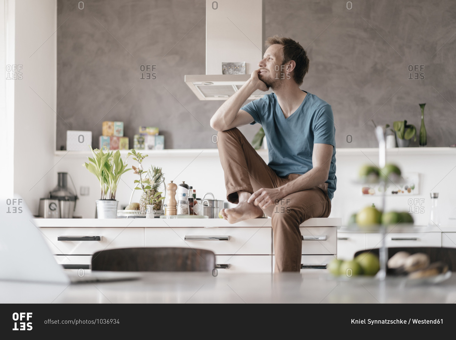 Smiling man sitting on kitchen counter looking at distance