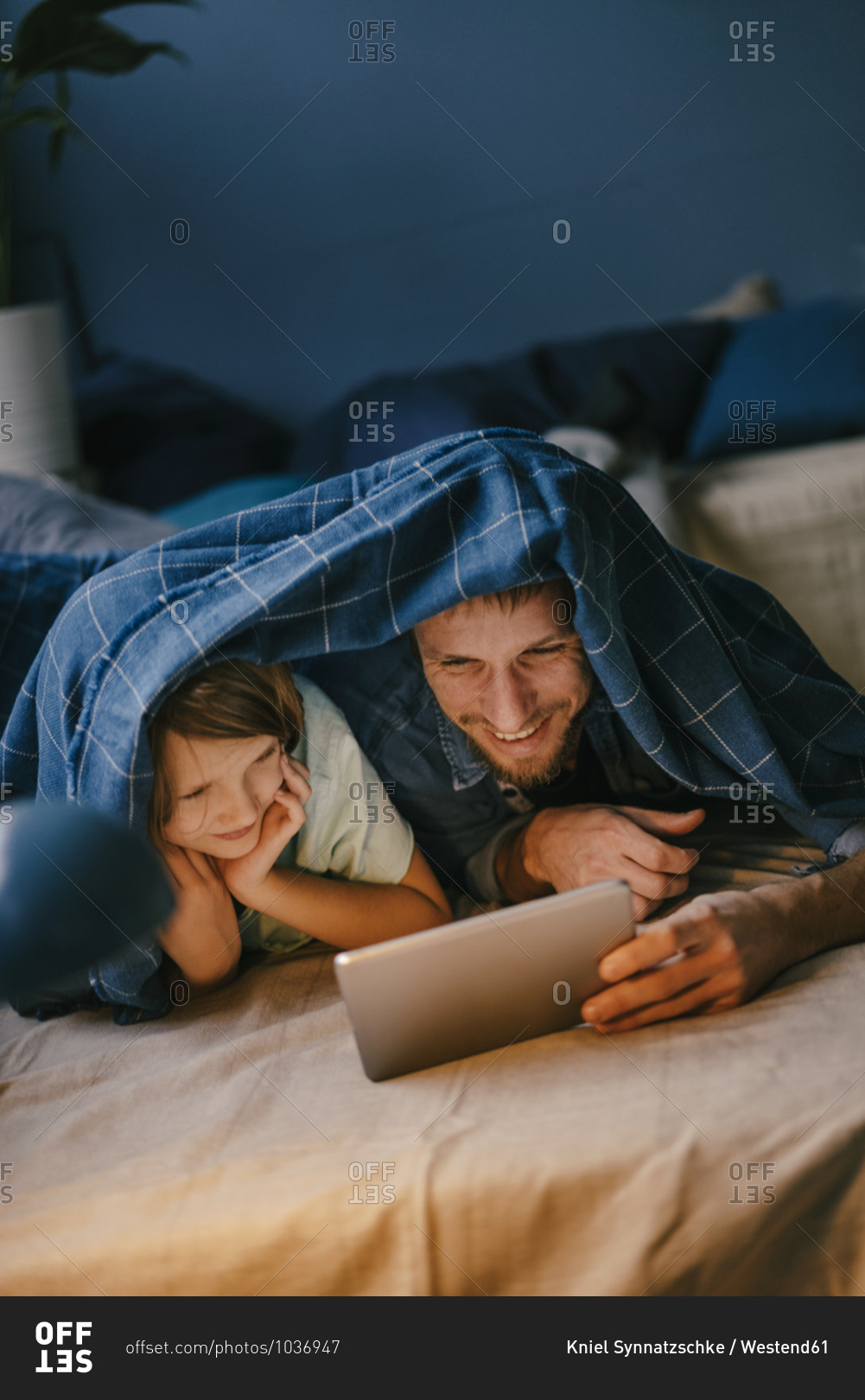 Happy father and son watching a movie on tablet under blanket
