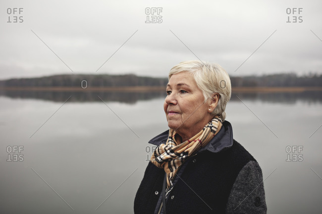 Smiling wrinkled woman looking away by lake against clear sky