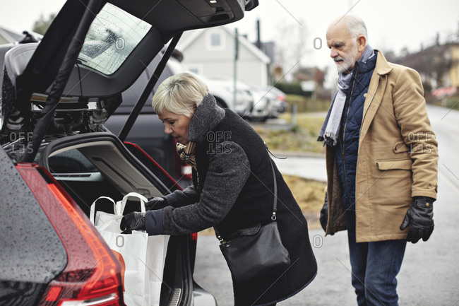 Senior man looking at partner standing by car trunk during winter
