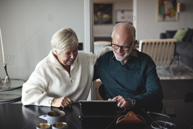 Smiling senior couple using digital tablet while sitting by dining table in living room