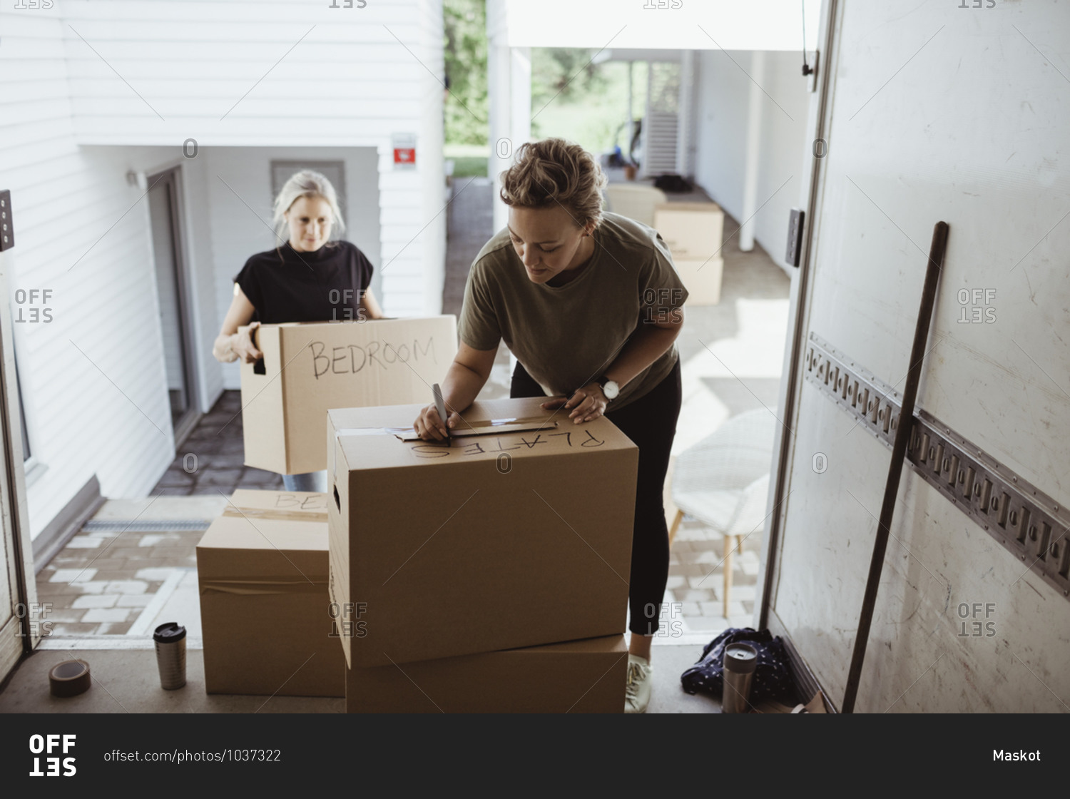 Woman holding box while female writing on cardboard box in moving van