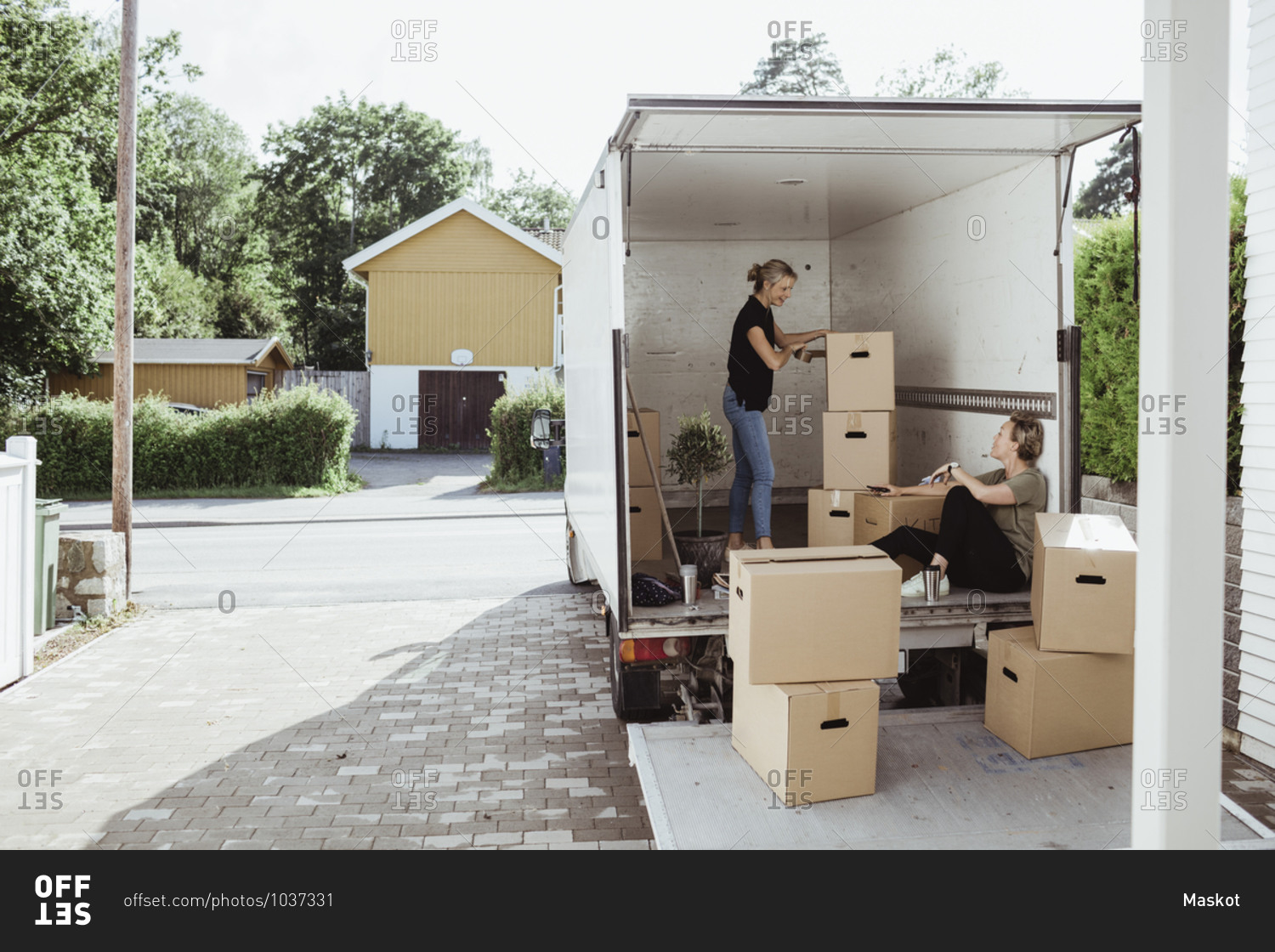 Side view of woman with boxes talking to female friend in moving van