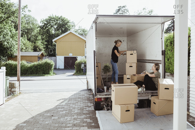Side view of woman with boxes talking to female friend in moving van