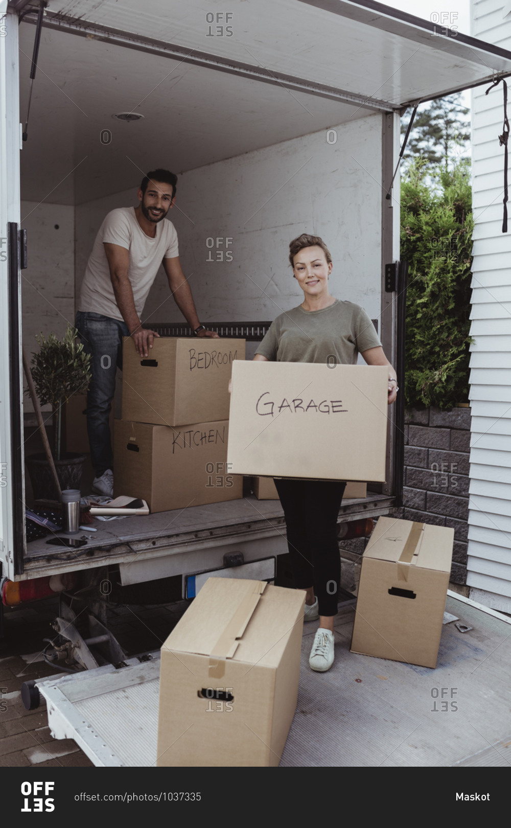 Portrait of smiling male and female partners unloading cardboard boxes from van