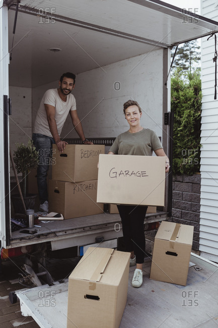 Portrait of smiling male and female partners unloading cardboard boxes from van
