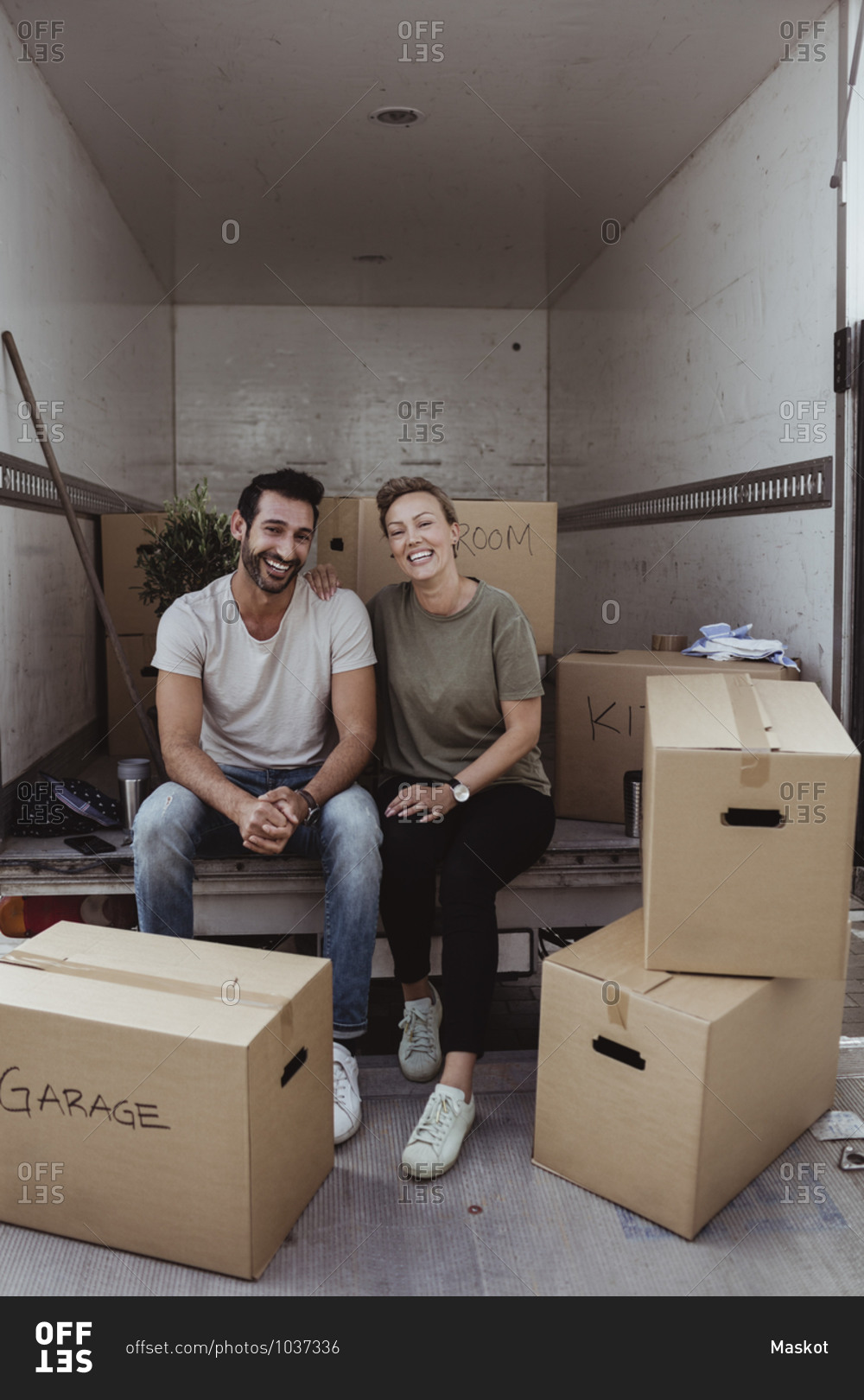 Portrait of smiling male and female partners sitting by cardboard boxes in van