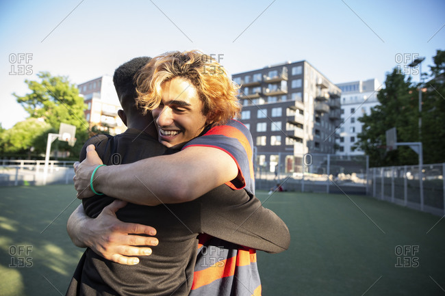 Happy friends embracing each other while playing in sports field