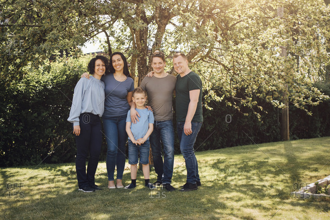 Portrait of smiling homosexual couples with son standing in backyard