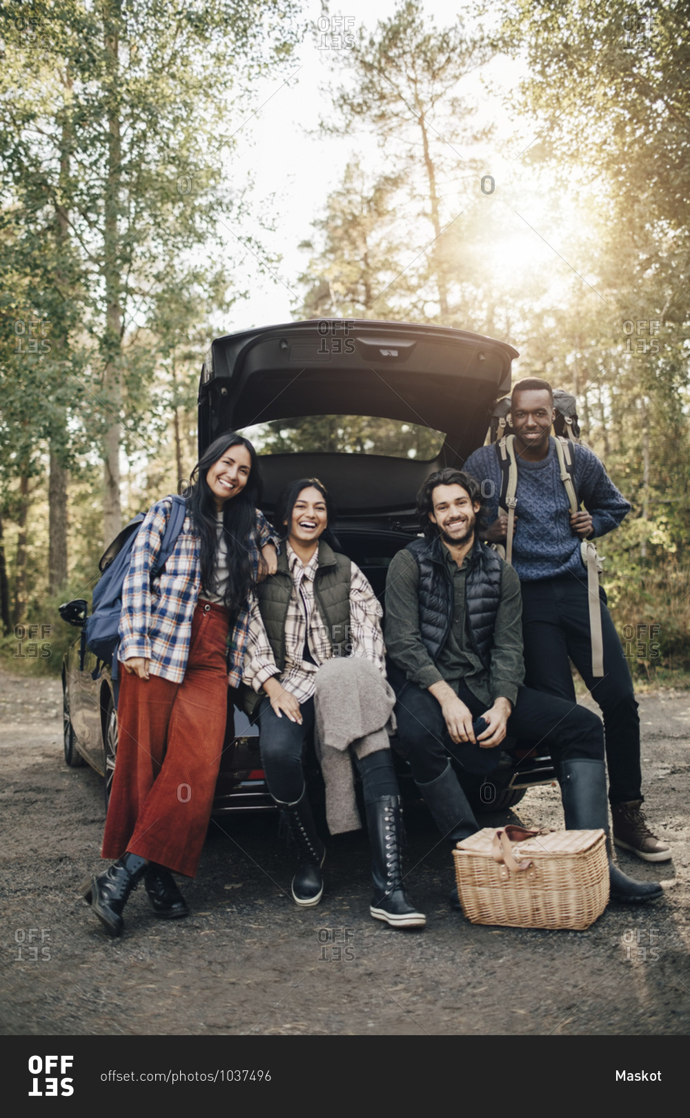 Portrait of smiling male and female friends sitting in car trunk during vacation
