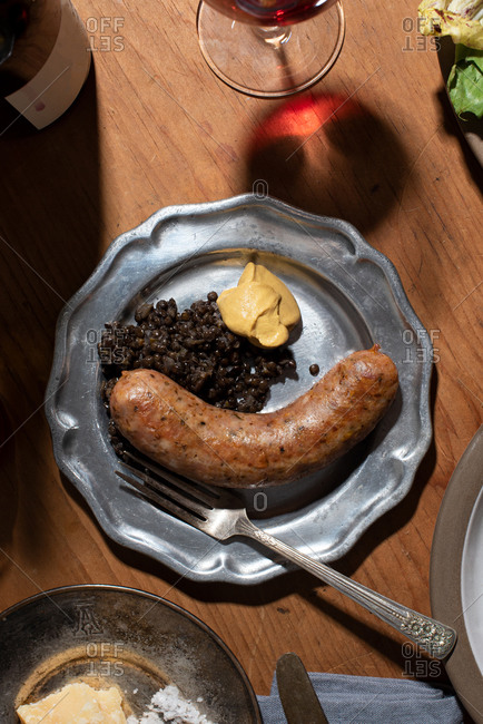 A sausage on a plate with mustard and lentils