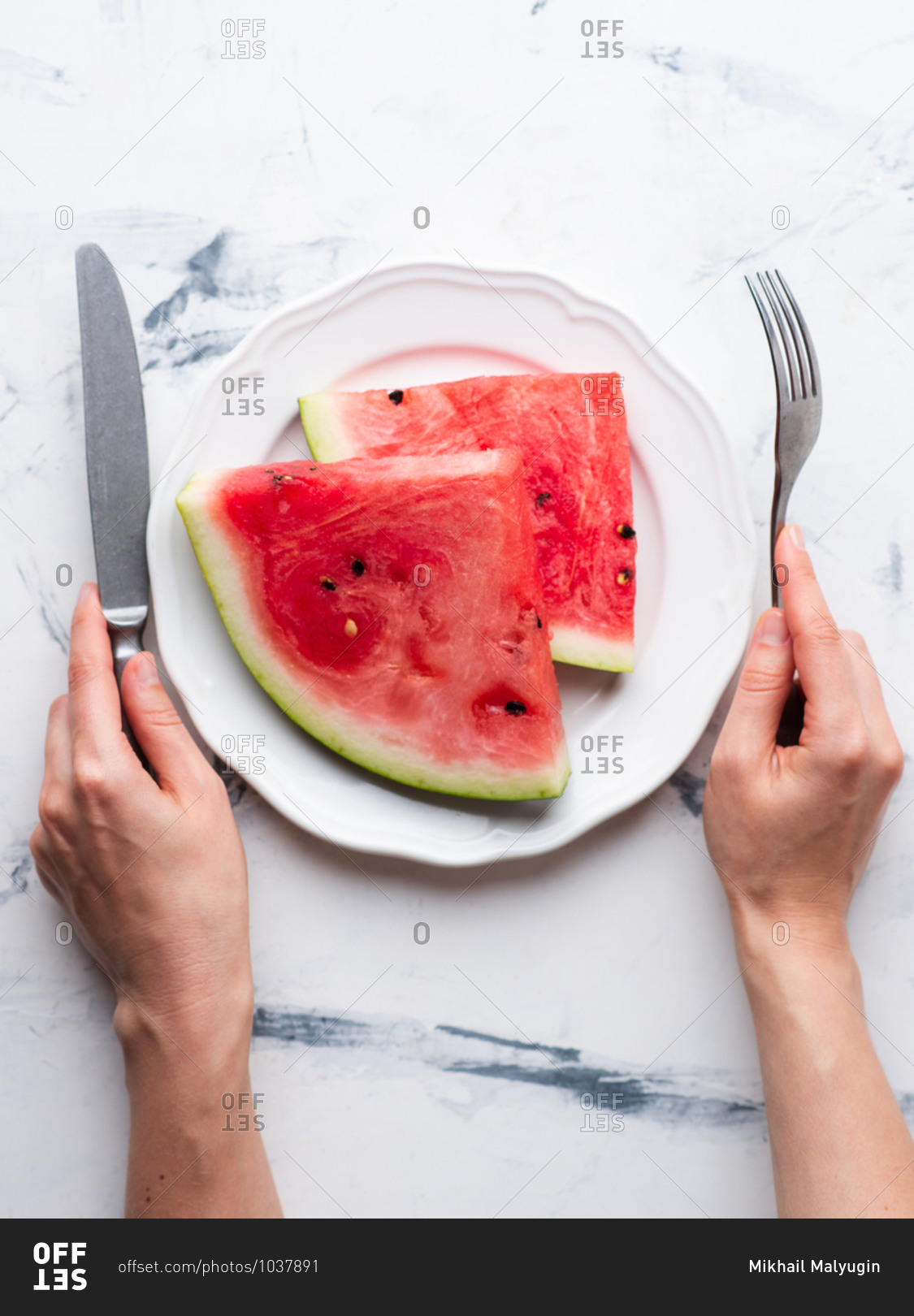 Sliced watermelon served on ceramic white plate over white background. Female hands holding fork and knife
